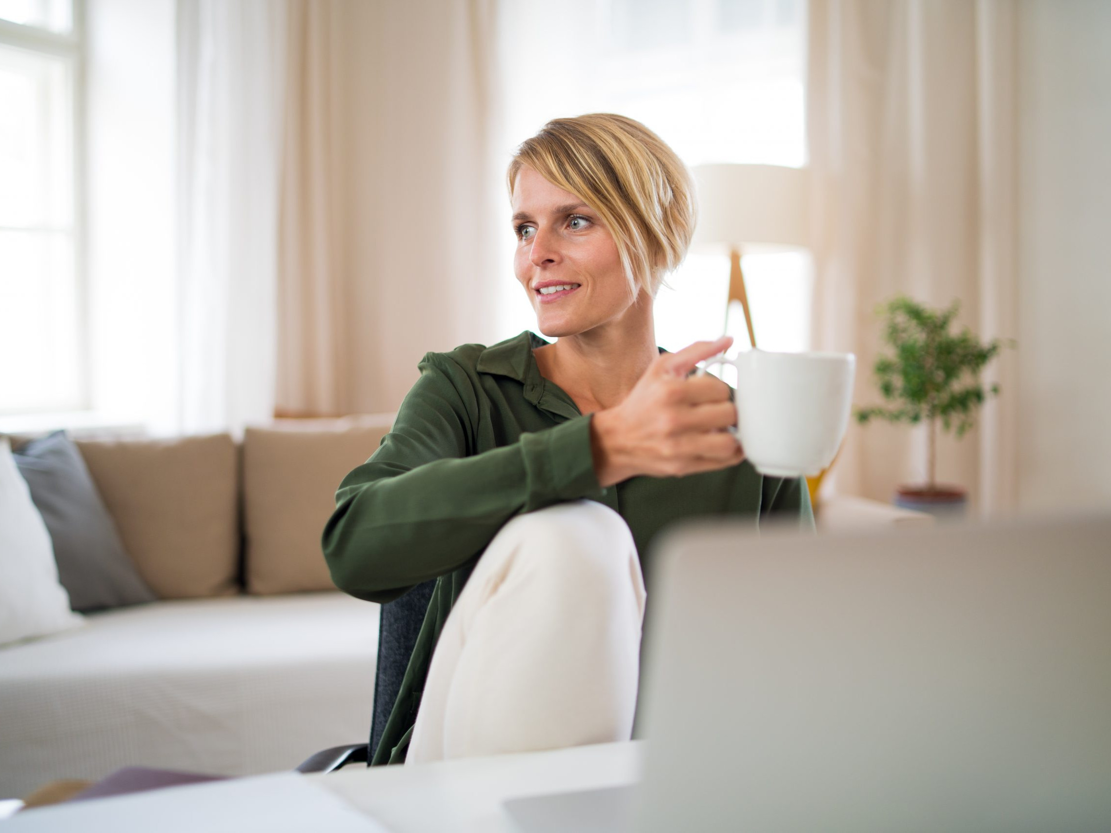 Portrait of business woman indoors in office sitting at desk, holding cup of tea.