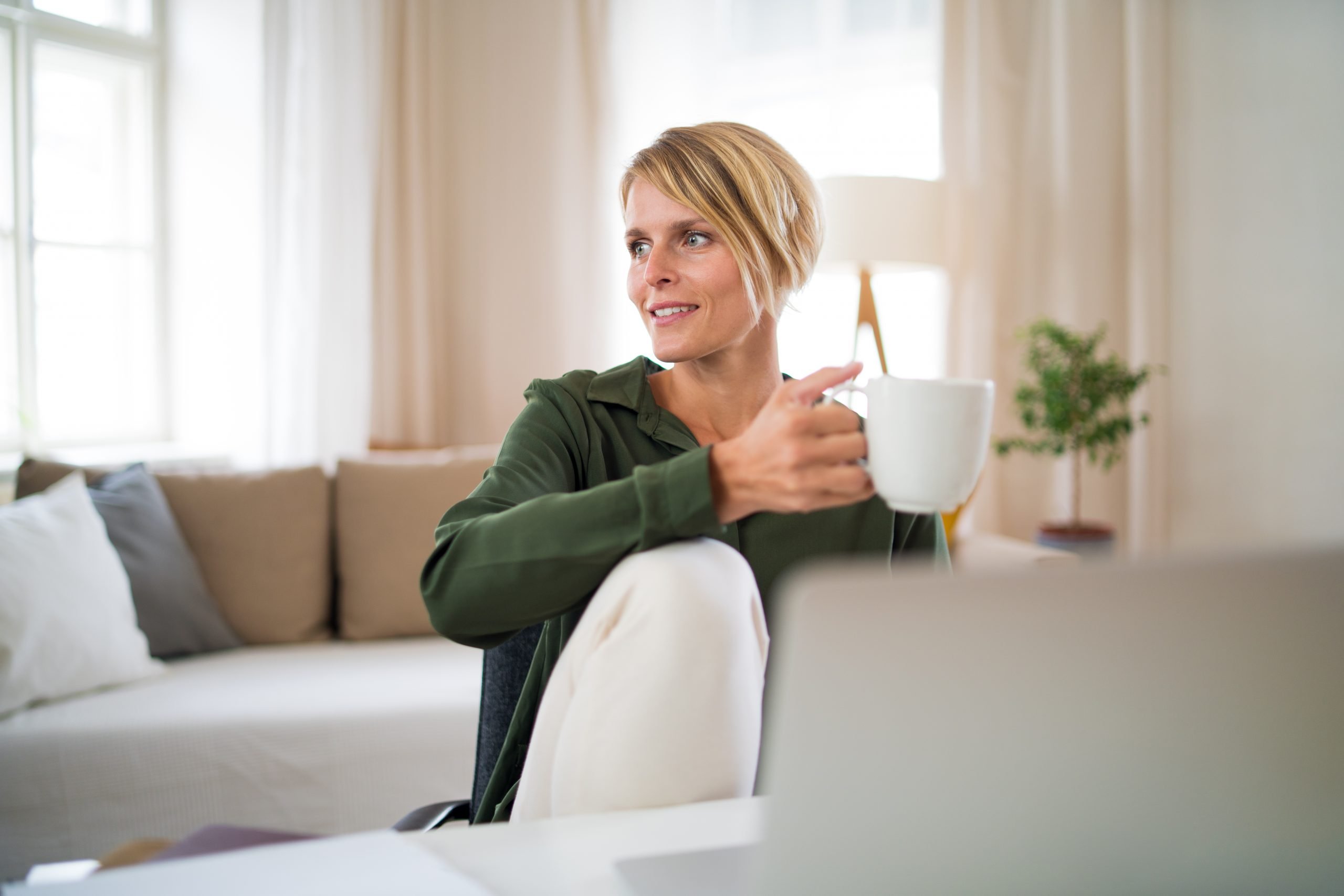 Portrait of business woman indoors in office sitting at desk, holding cup of tea.