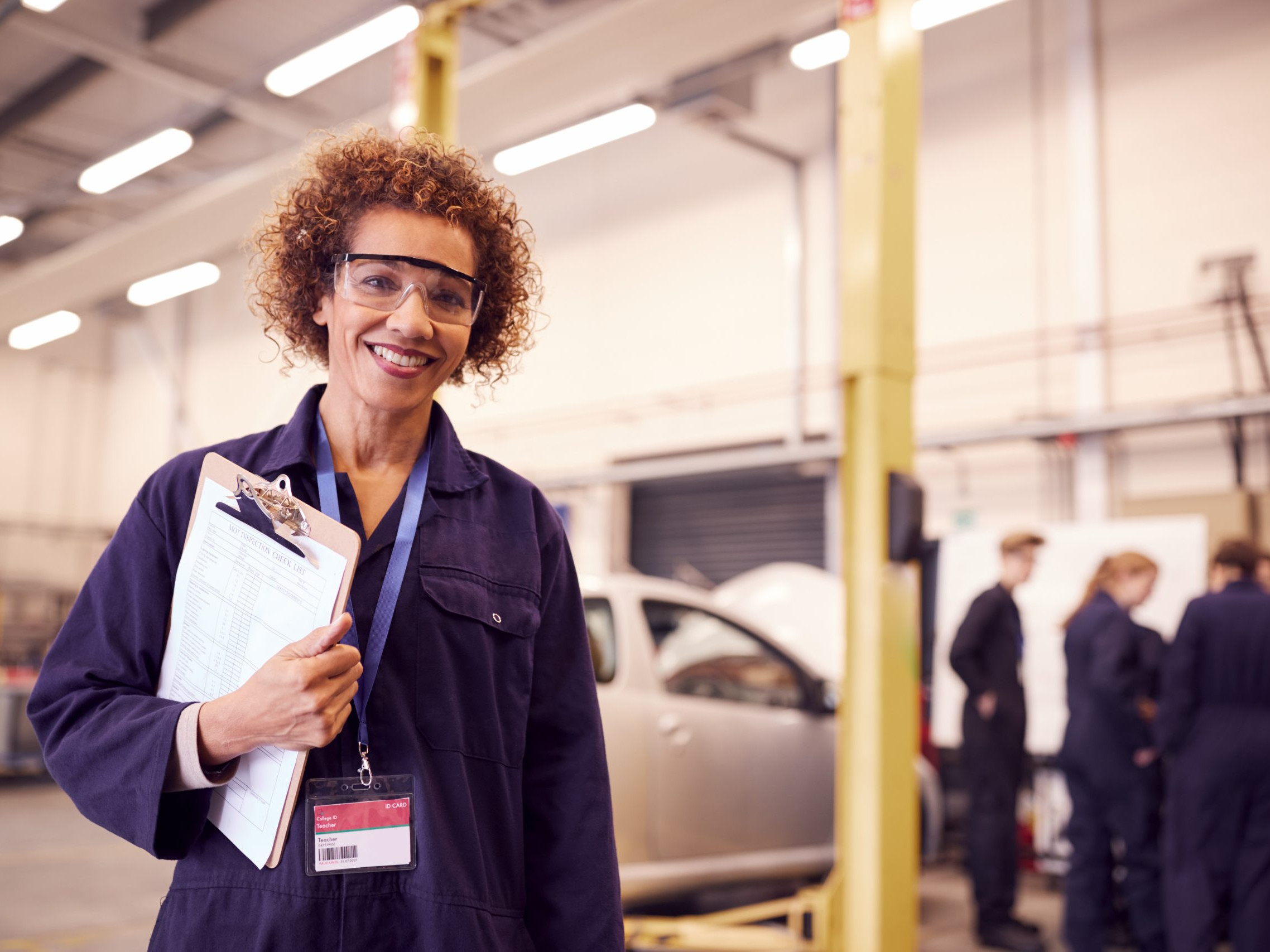 Portrait Of Female Tutor With Safety Glasses Teaching Auto Mechanic Apprenticeship At College